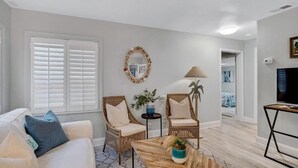 A living room with a white sofa, two wicker chairs, a coffee table, and a TV on a stand. - Key Lime Cottage - Updated - 1 Minute Walk to Beach & Pier (Flagler Beach)