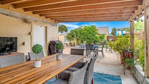 A covered patio area with a wooden table and chairs, potted plants, and a view of neighboring houses. - Key Lime Cottage - Updated - 1 Minute Walk to Beach & Pier (Flagler Beach)