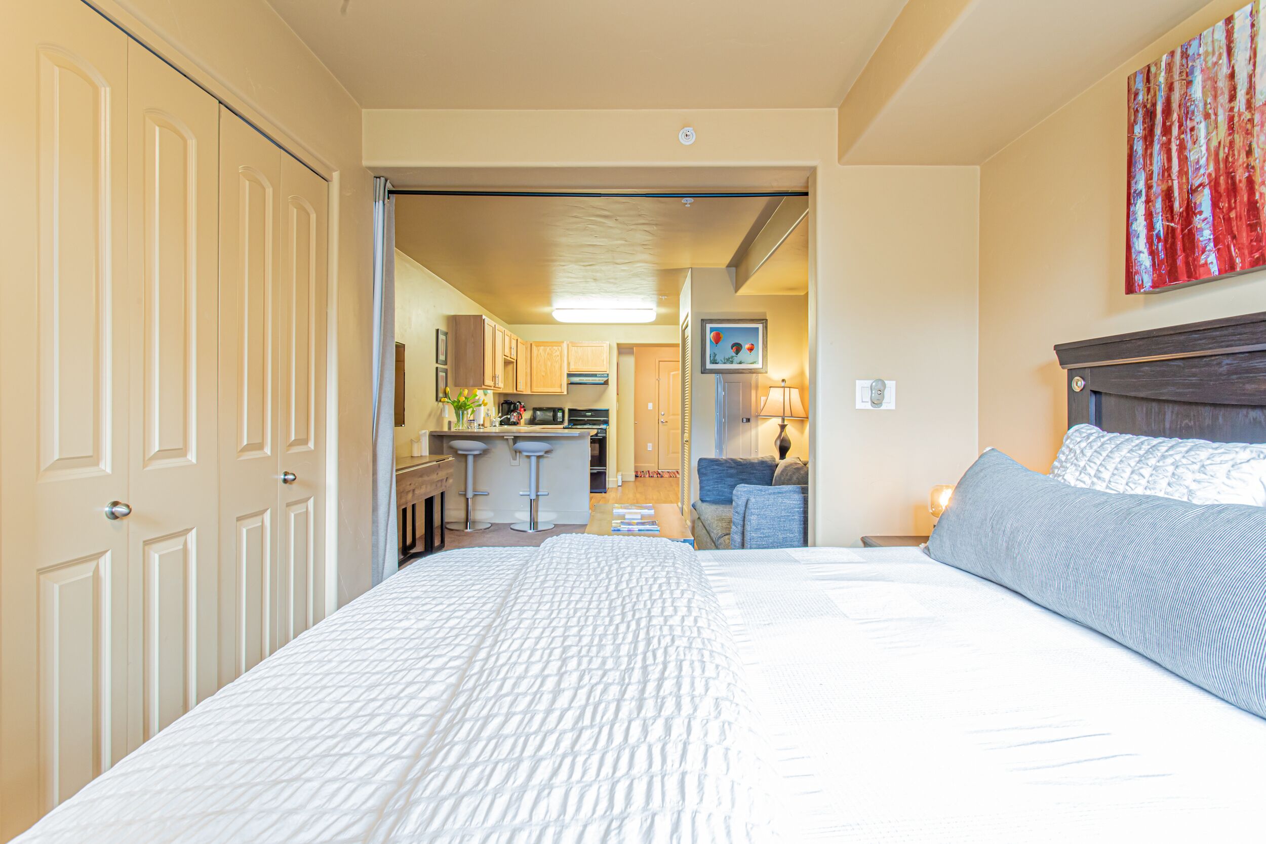 A hotel room with a large bed, a desk, and a kitchenette in the background.