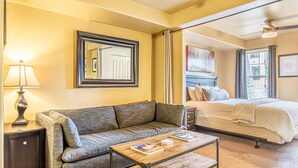 Een kamer met een bank, een bijzettafeltje met boeken, een bed, een nachtkastje, een lamp en een grote spiegel.