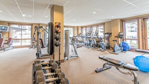 Een sportschool met diverse fitnessapparaten, grote ramen en een vloerbedekking.