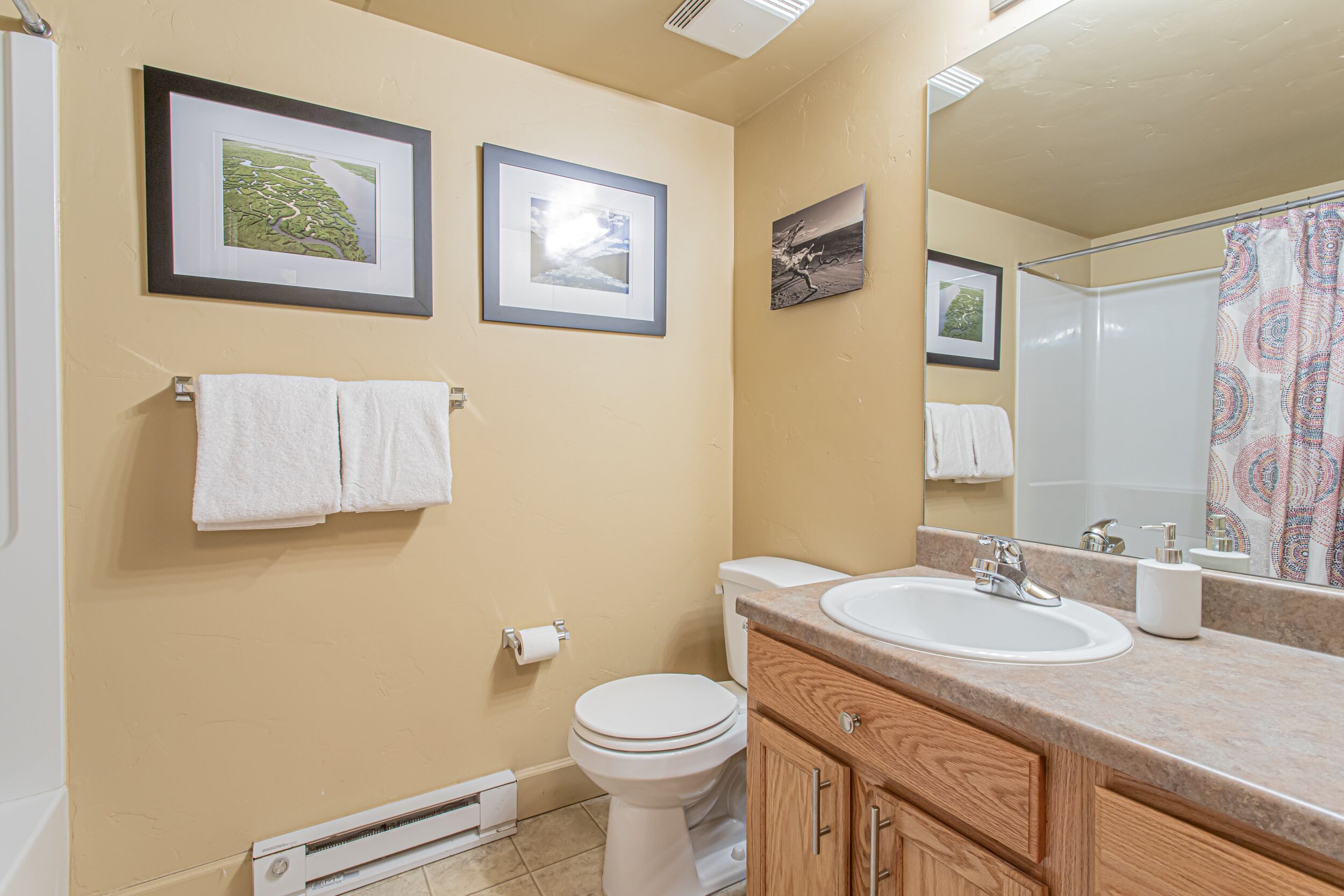 A bathroom with a toilet, sink, and mirror. There are framed pictures on the wall and a towel rack with towels.