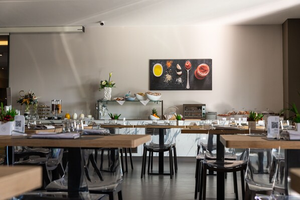 A modern dining area with tables, chairs, and a kitchen in the background. - Building Hotel (Carinaro)