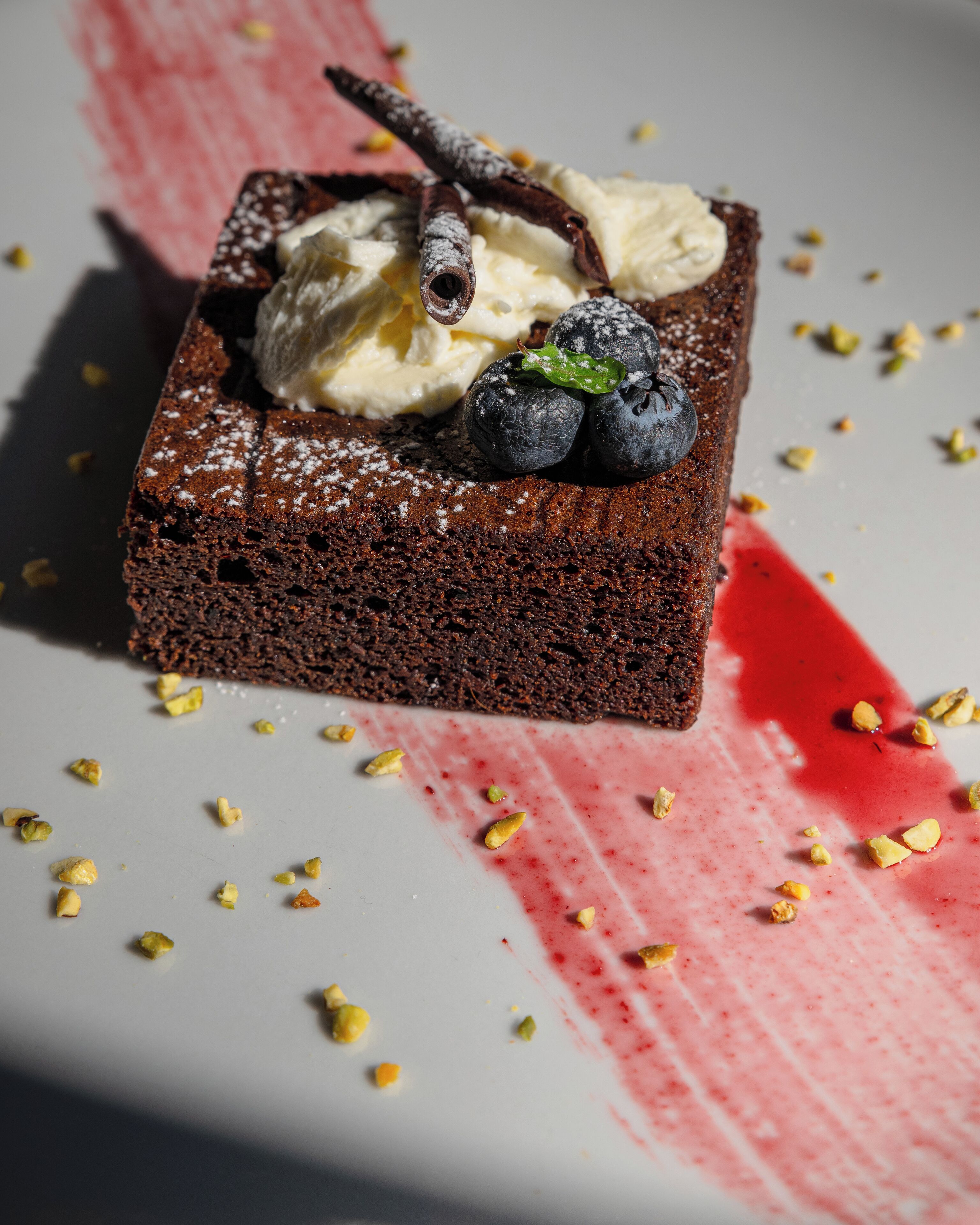 A dessert with chocolate cake, ice cream, and blueberries on a plate with scattered nuts.