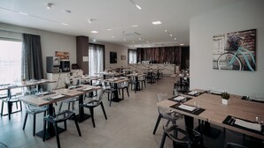 A modern dining area with multiple tables and chairs, a kitchen area, and a large window with curtains. - Building Hotel (Carinaro)