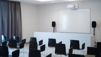 Une salle de conférence équipée d’un tableau blanc, de deux haut-parleurs et de rangées de chaises noires.