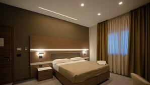A modern hotel room with a large bed, bedside tables, a nightstand, and a window with curtains. - Building Hotel (Carinaro)