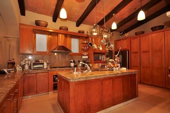 A spacious kitchen with wooden cabinets, a central island, hanging pots, and a brick ceiling.