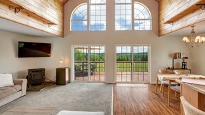 A spacious living area with a fireplace, a television, and a large window overlooking a scenic landscape. - Hilltop Country Home with Panoramic Views – Peaceful and Private Retreat (Walton)
