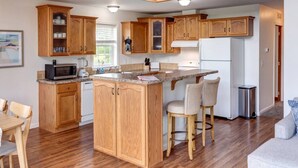 A kitchen with wooden cabinets, a granite countertop, a built-in island, a refrigerator, and a dining area with chairs. - Hilltop Country Home with Panoramic Views – Peaceful and Private Retreat (Walton)