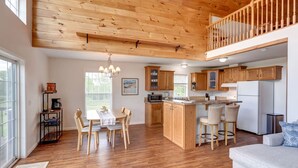 A spacious kitchen with wooden cabinets, a dining area with a table and chairs, a built-in island with bar stools, and a lofted seating area. - Hilltop Country Home with Panoramic Views – Peaceful and Private Retreat (Walton)