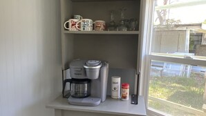 Une petite cuisine équipée d’une machine à café, d’un récipient à sucre et d’un bocal en verre posé sur le comptoir.