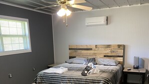 Une chambre à coucher avec une tête de lit en bois, un lit avec une literie à rayures, un ventilateur de plafond et une fenêtre avec des stores.