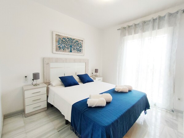 Une chambre d’hôtel comprenant un lit, des tables de chevet, une commode, un téléphone fixé au mur, une fenêtre avec des rideaux et un tableau encadré.