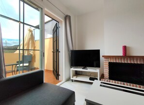 Un salon équipé d’un téléviseur, d’une cheminée, d’un balcon avec une chaise et une table, et d’une porte-fenêtre coulissante.