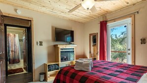 Een slaapkamer met een bed, een televisie, een houten plank en een raam met gordijnen.