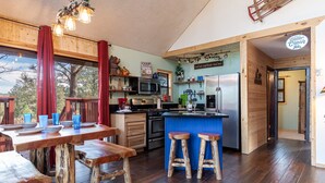 Een interieur van een blokhut met een houten eettafel, barstoelen, een keuken met een koelkast, en een bordje met de tekst 'Better Cabin'.