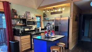 Een moderne keuken met een centraal eiland, houten krukken, een roestvrijstalen koelkast en een magnetron.