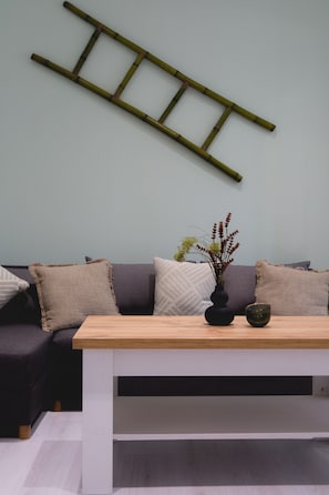 Una sala de estar moderna con una mesa de centro de madera, un jarrón oscuro con plantas secas y una escalera fijada a la pared.
