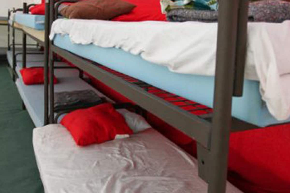 Un lit superposé avec une literie rouge et blanche, un matelas gris et un sol vert.