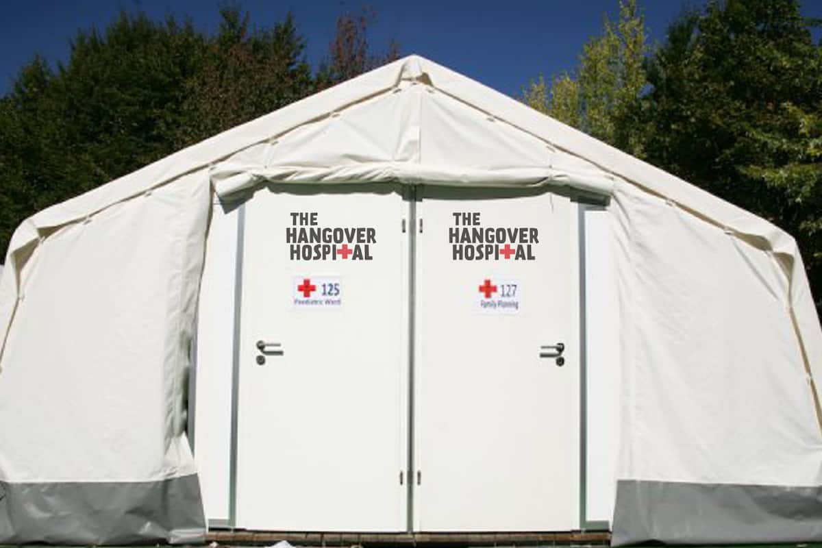 Une tente blanche avec une enseigne indiquant « The Hangover Hospital » et des numéros de téléphone d’urgence.