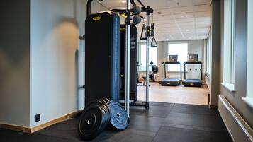 Ett gym med en tyngdlyftningsstation, löpband och ett stort fönster som släpper in naturligt ljus.