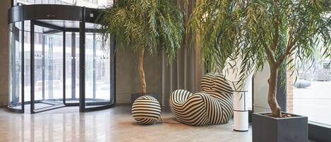 A modern lobby with a revolving door, potted plants, and striped seating.