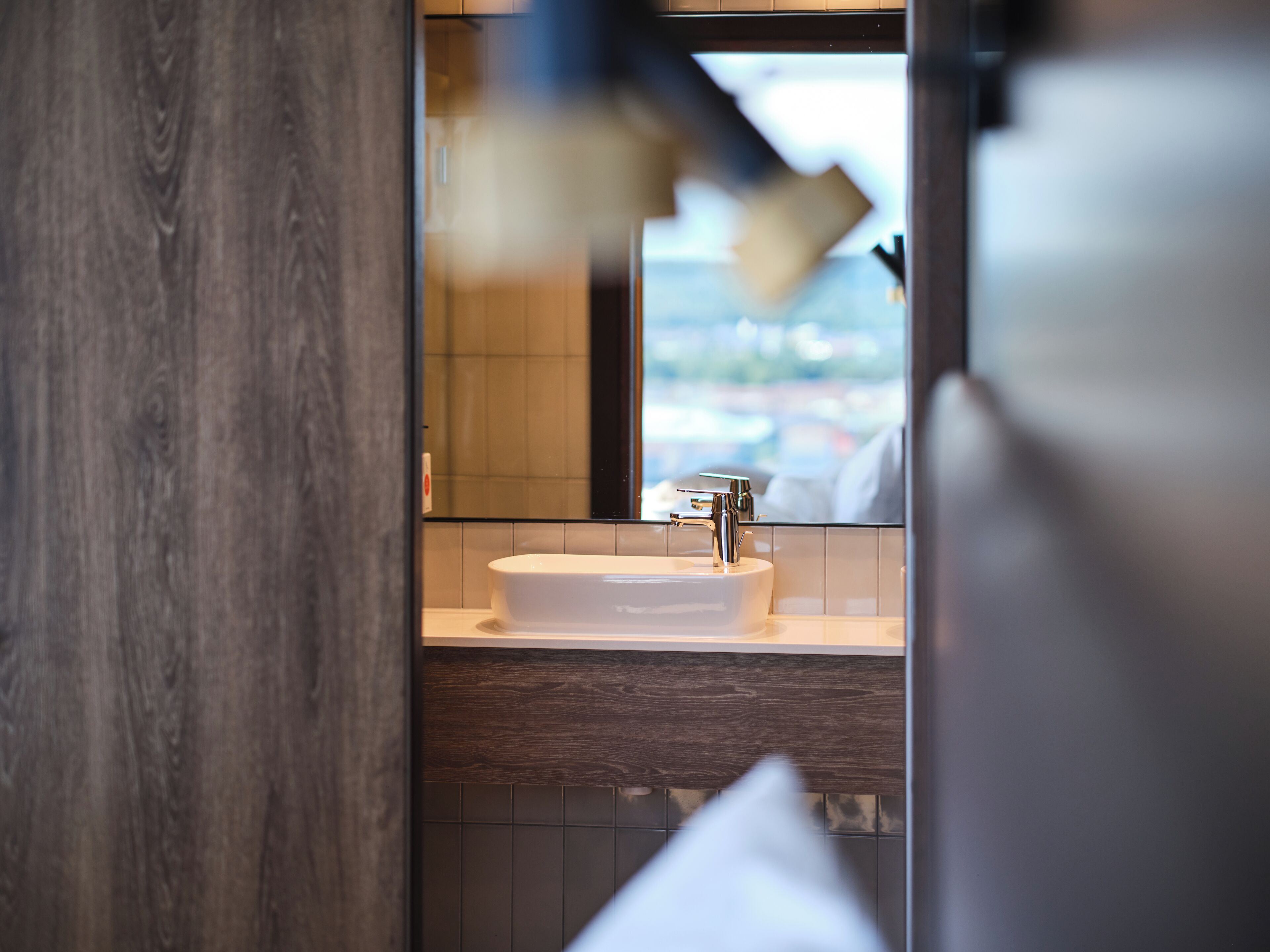 Une salle de bain moderne avec un lavabo blanc, un meuble-lavabo en bois et une vue par la fenêtre.