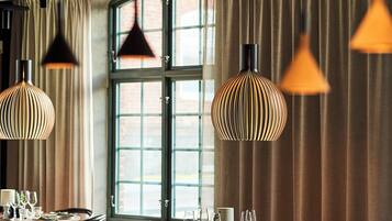 A dining area with a table set for a meal, a window with curtains, and pendant lights.