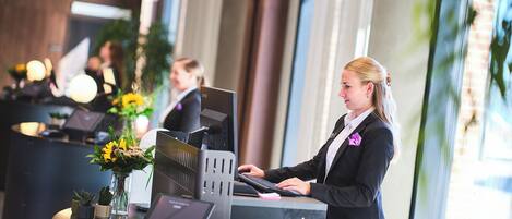 A reception desk with a computer, a cash register, and a credit card reader. There are potted plants on the counter.