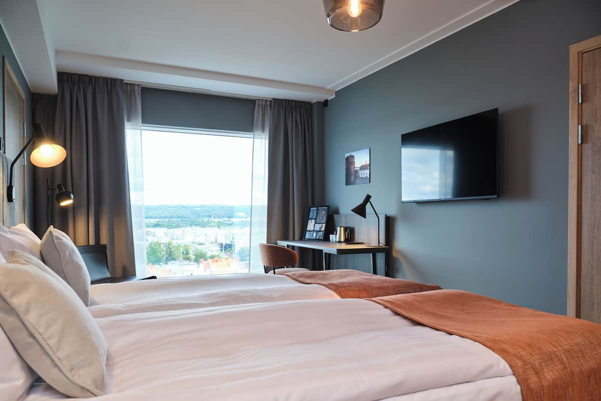 Une chambre d’hôtel moderne dotée d’un grand lit, d’un bureau, d’une télévision à écran plat et offrant une vue sur la ville.