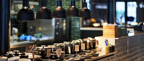 A kitchen counter with various cooking utensils and containers, a window with a view of the city, and hanging kitchen lights.
