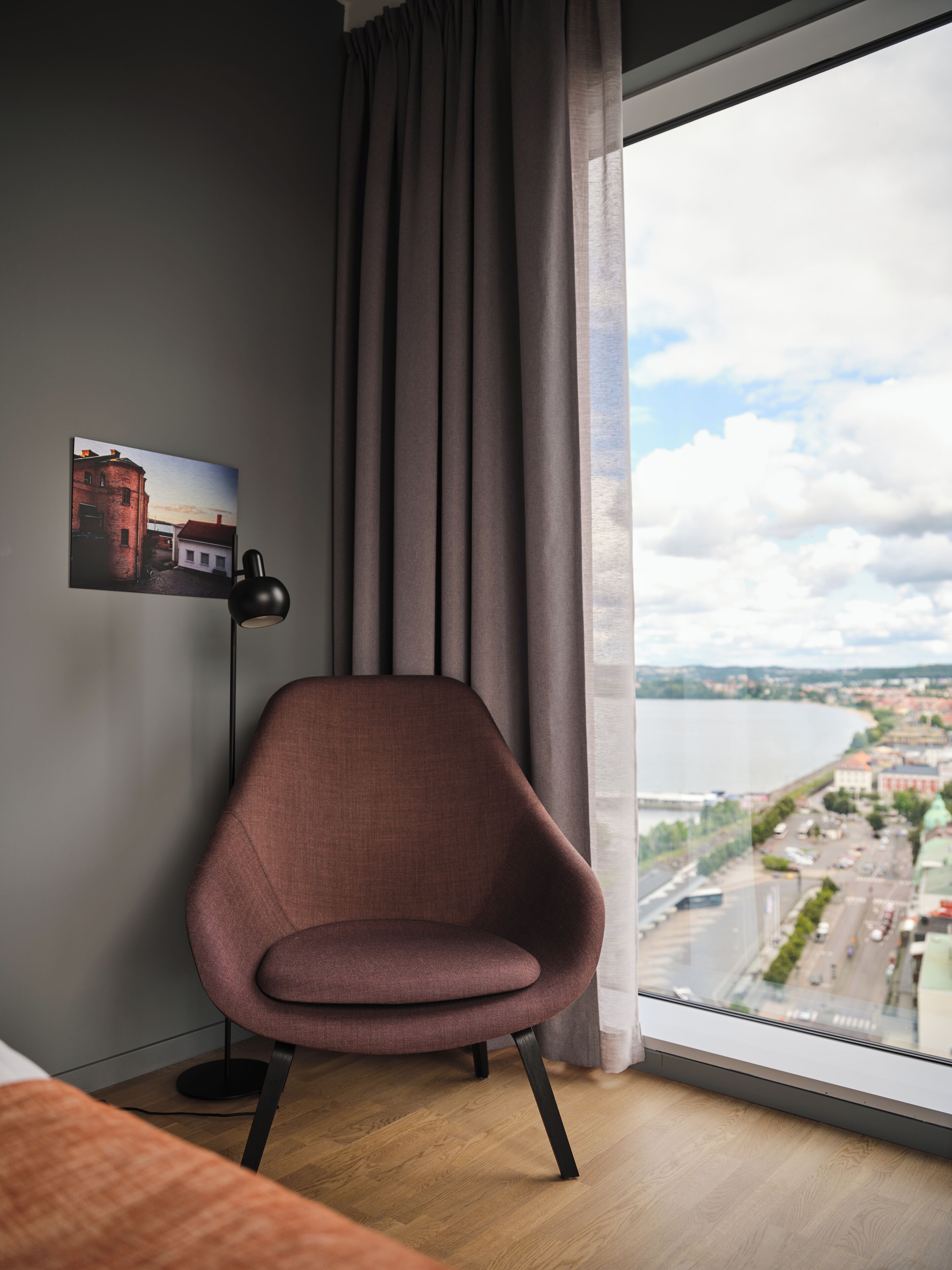 Een moderne kamer met een groot raam, een stoel, een vloerlamp en een schilderij aan de muur.