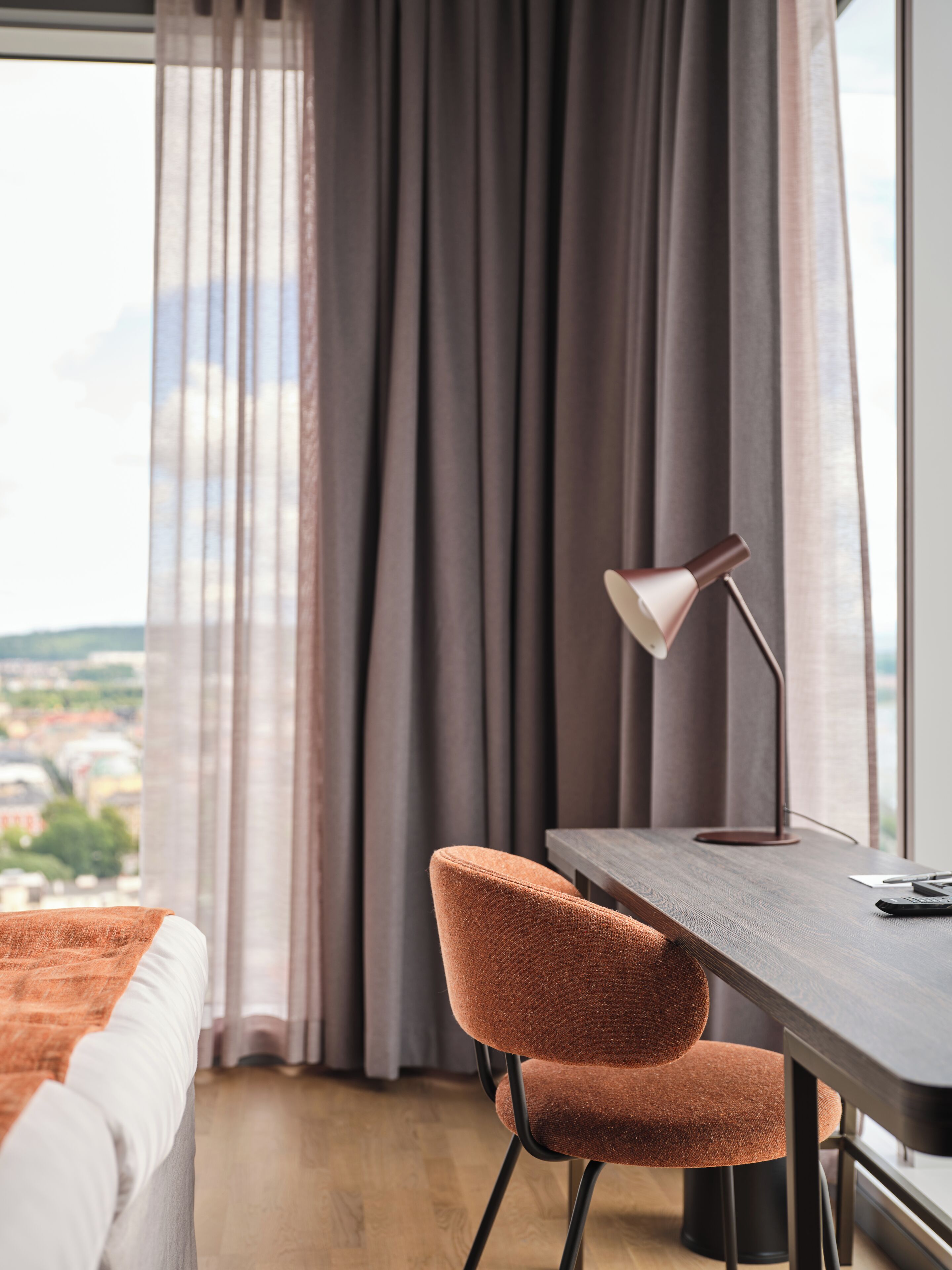 A modern bedroom with a large window, a desk with a lamp, and a chair.