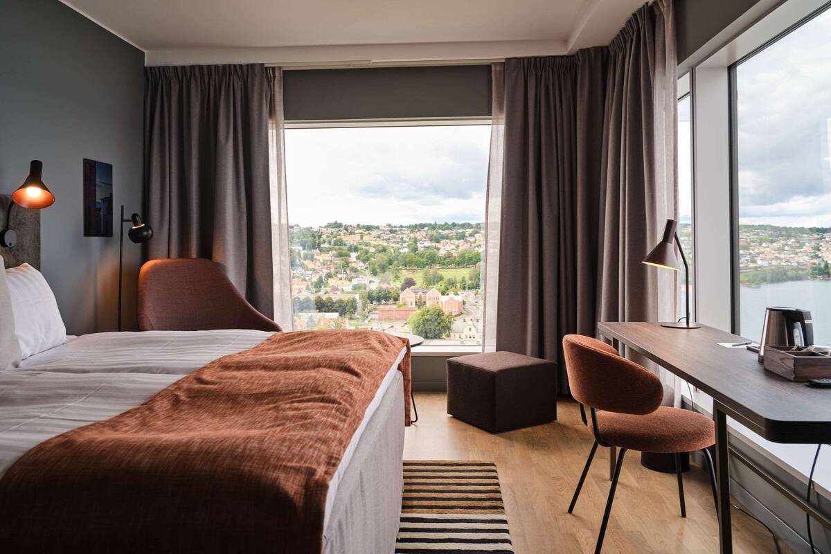 Une chambre d’hôtel avec un lit, un bureau, une chaise et une vue sur le paysage urbain.