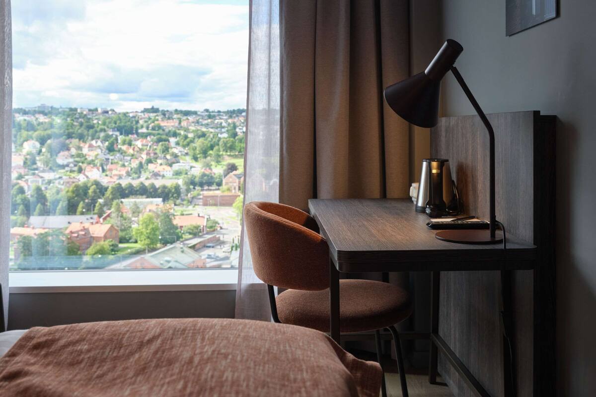 Une chambre d’hôtel avec un lit, un bureau doté d’une lampe et une vue sur la ville par la fenêtre.