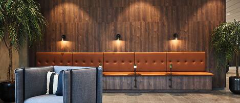 A modern lobby with a wooden wall, a sofa, a chair, and two potted plants.