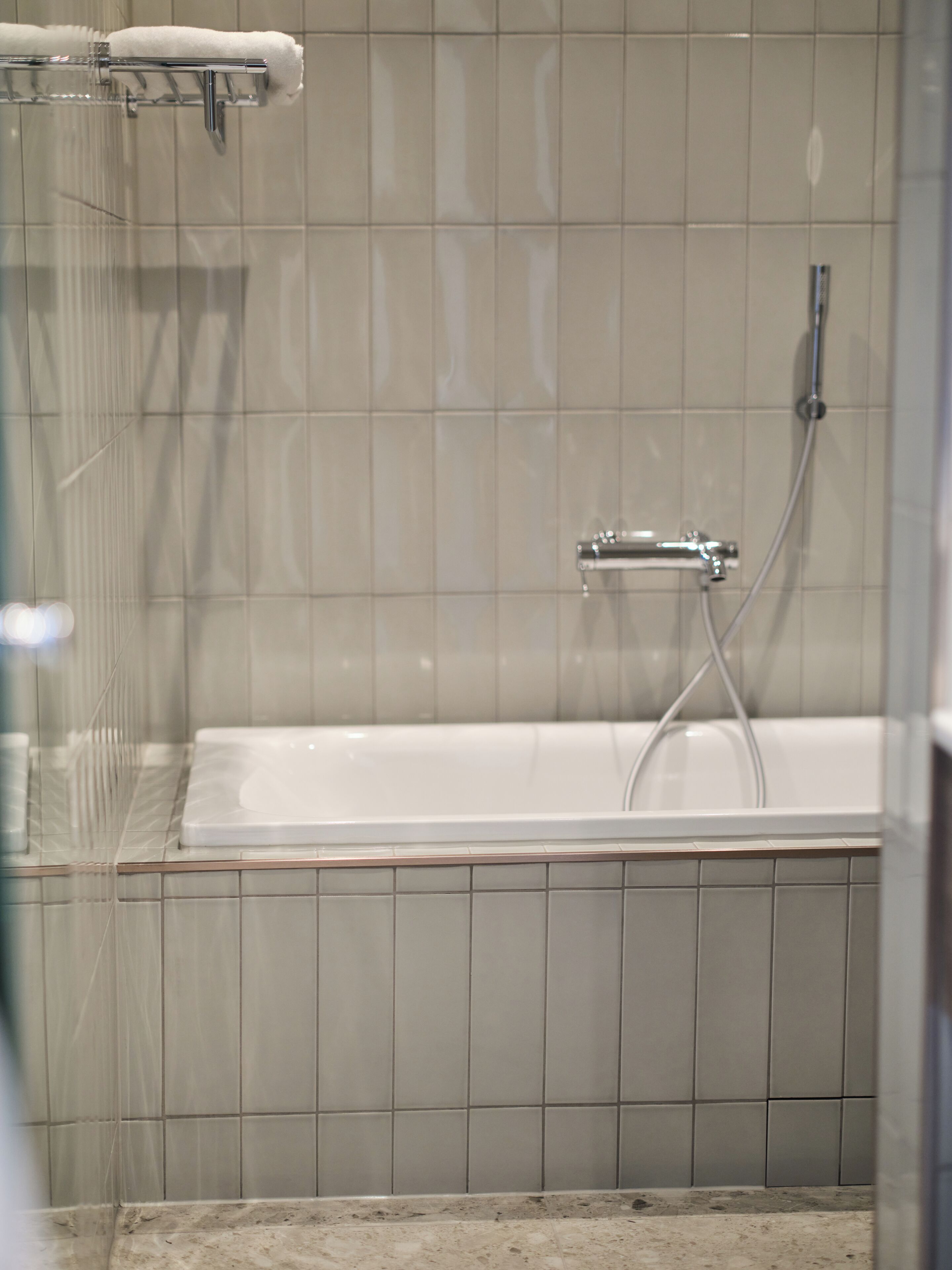 A bathroom with a glass shower enclosure, a white bathtub, and a tiled wall.