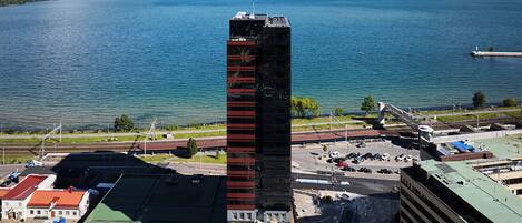 A tall building with a modern design, situated near a body of water and a parking area.