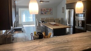 Cozinha moderna com ilha central, eletrodomésticos de aço inoxidável, luminárias pendentes e área de refeições com cadeiras.