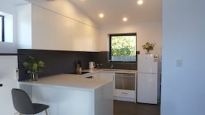 A modern kitchen with white cabinetry, a central island, a window with a view, and a refrigerator. - Situated across the road from the beach (Bridport)