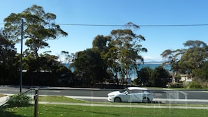A white car parked on a grassy area beside a road with trees and a clear sky. - Situated across the road from the beach (Bridport)