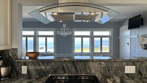 Una cocina con una isla grande, una estufa a gas y vistas al océano a través de amplias ventanas.