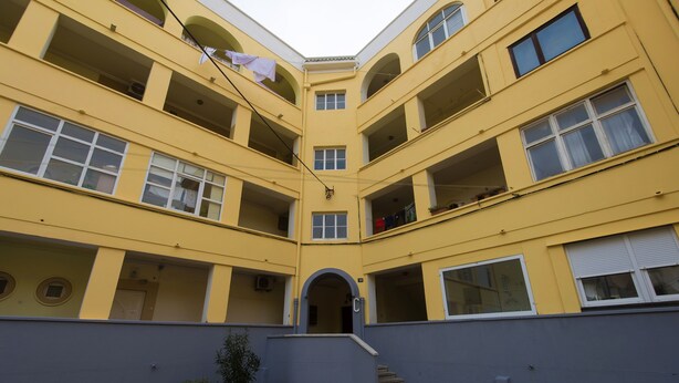 Un immeuble jaune à plusieurs étages, doté de balcons, d’une entrée centrale et d’un mur extérieur bleu.
