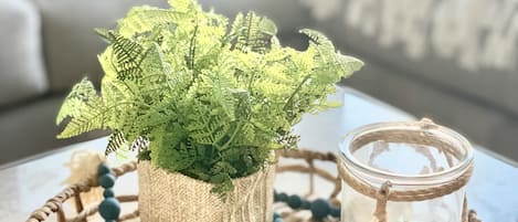 A woven tray with a potted fern, a beaded necklace, a small jar, and a textured stone.