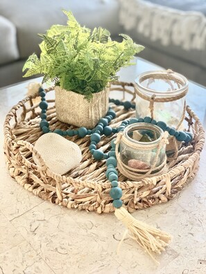 A woven tray with a potted fern, a beaded necklace, a small jar, and a textured stone. - Coco Bay • 4 Min Walk to Beach & Tiki Bar • Rooftop Ocean Views • Sleeps 12 (Carolina Beach)