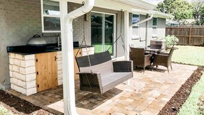 Eine überdachte Terrasse mit Grill, Sitzgelegenheiten und einer Hängematte.