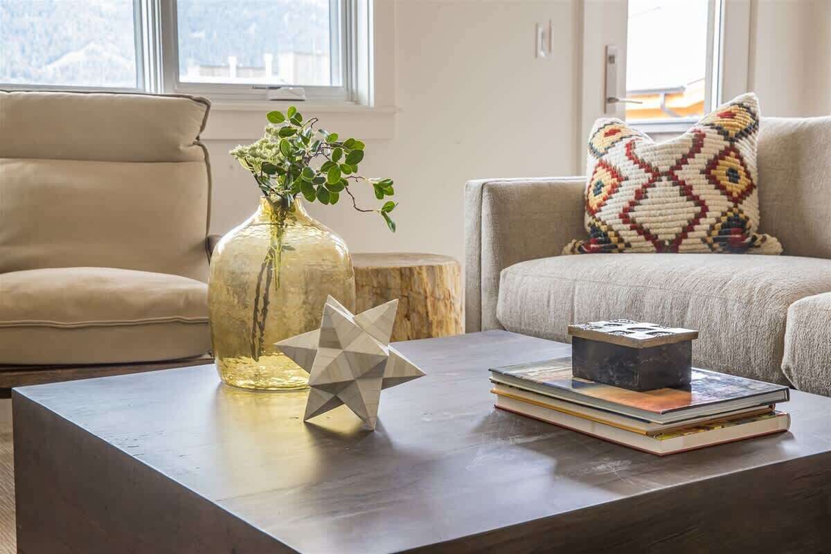 Un salon moderne avec un canapé, une table basse ornée d’un vase et d’une sculpture géométrique, et un coussin à motifs.