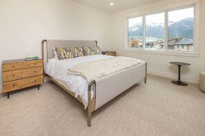 A bedroom with a bed, wooden nightstands, a small round table, and a large window with a mountain view.
