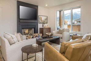Ein modernes Wohnzimmer mit Kamin, großem Fernseher und Bergblick durch große Fenster.